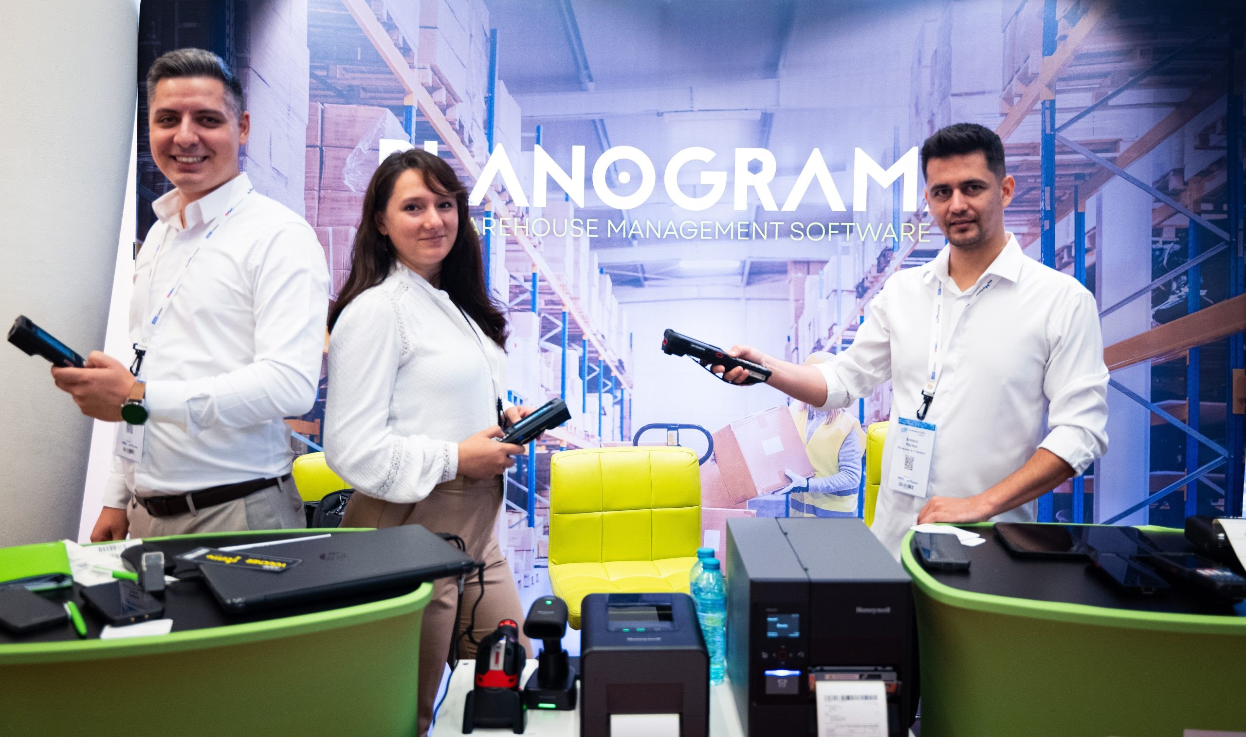 Three people staffing the Planograma booth at eCommerce Talks, holding handheld mobile computers, with Honeywell label printers and barcode scanners on the counter